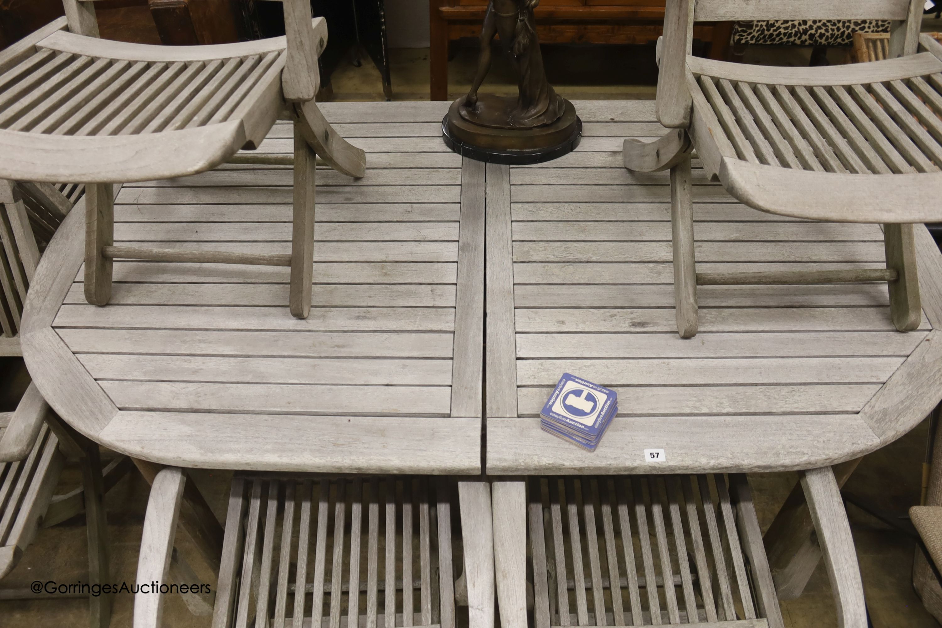 A weathered teak extending garden table, diameter 128cm, height 68cm and six folding elbow chairs